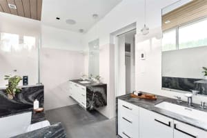 A modern bathroom with sleek marble countertops and flooring, featuring a minimalist design with white cabinetry and pendant 