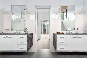 Modern bathroom with marble countertops, white cabinets, and large mirrors.