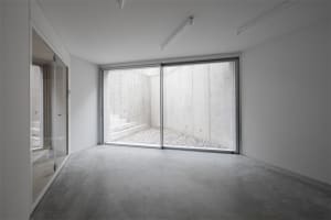 A minimalist space with a concrete ground and wall, featuring a view of a gravel courtyard and steps leading downwards.