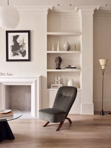 A minimalist living room with a dark gray chair, white open shelves, and a wooden floor.