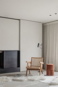 A minimalist living room with a wooden armchair, a floor lamp, and a white fur rug.