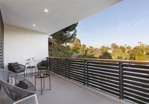 A modern balcony featuring a wooden and metal railing with a view of trees and sky.
