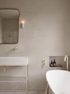 A minimalist modern bathroom with concrete walls and floors, a white sink, and a freestanding bathtub.