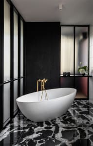 A modern bathroom with a white oval bathtub, gold faucets, and a black and white marble floor.