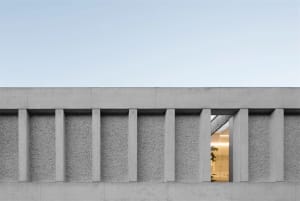 A modern building exterior with concrete pillars and a view into a well-lit interior space.