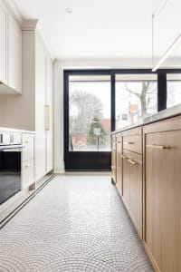 A modern kitchen featuring a tile floor with a wave pattern, wooden cabinets with brass handles, and large windows with a vie