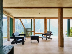 Modern minimalist living room with wooden furniture and large windows overlooking a scenic outdoor view.