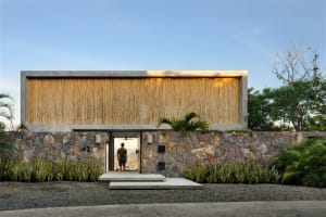 A modern residential entry with a wooden wall and concrete base, featuring a person standing inside the doorway.
