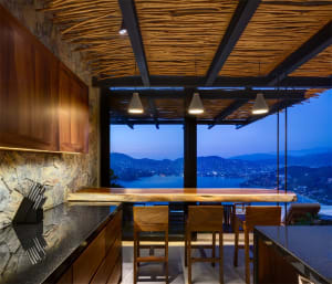 Modern minimalist residential interior with wood elements and a view of mountains and water at dusk.