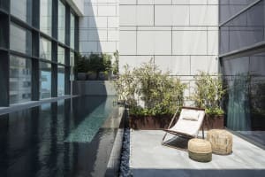 Concrete rooftop pool with glass walls, lounge chair and potted plants