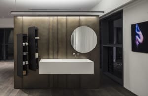 Modern bathroom suite with minimalist design featuring metallic paneling, floating sink, and large round mirror.