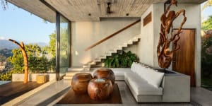 A modern residential living room featuring concrete floors, a white sofa, and wooden furniture and sculptures.
