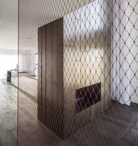 A modern living room with a glass fireplace and red wire mesh partition.