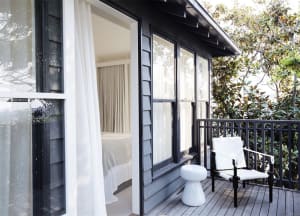 A modern veranda with wooden materials, offering a view into a cozy bedroom with a bed and curtains.