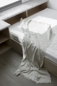A minimalistic bedroom with a cotton-blend blanket draped over the bed.