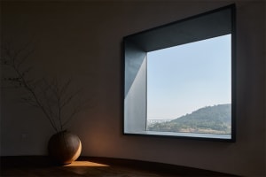 A minimalist living room with a concrete floor and large window overlooking distant hills.