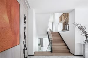 Modern interior space featuring a white staircase with wooden railing and a large orange artwork mounted on the wall.