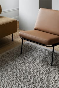 A minimalist living room featuring a stylish leather chair with metal frame on a textured rug.