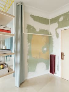 A wall undergoing renovation with peeling wallpaper and exposed underlying surface.