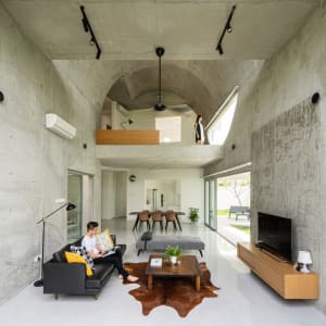 A minimalist living room with concrete walls, wood accents, and a black sofa with multicolored pillows.