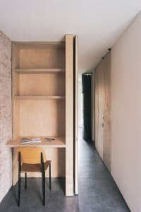A minimalist home office featuring a wooden desk and chair, with shelves and a door for organization.
