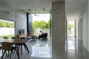 A modern living room with concrete walls, a dining area, and a view of the garden.