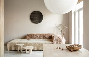 A minimalist living room features a cozy couch draped in natural fiber material and a wooden dining table with a bowl of nuts