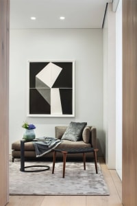 A minimalist living room with a gray sofa, geometric artwork, and modern side table.