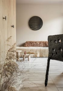 A modern living room with wooden furniture and a fluffy blanket on the couch, featuring a round mirror on the wall and a wood
