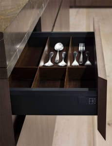 A drawer with cutlery organized in compartments, featuring dark wood material.