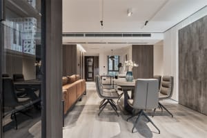 A modern residential dining room with a wooden floor, a brown leather sofa, and grey chairs. The room features contemporary d