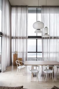 A modern residential dining room with white chairs, a wooden table, and sheer curtains allowing natural light to fill the spa