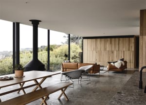 A modern living room with wood-paneled walls and a concrete floor, featuring a black fireplace, two leather sofas, a wooden d