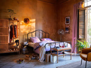An industrial-style bedroom with a metal bed frame, wooden wardrobe, and concrete walls.