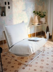 A minimalist living room with fabric cushions on a white metal chair.