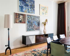 A modern living room featuring abstract paintings on the wall, a wooden floor, and a colorful rug.