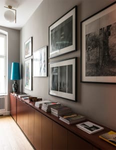 A modern interior entryway featuring wooden cabinets, framed photographs on the wall, and a teal lamp.