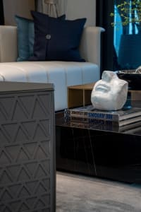 A modern living room featuring marble coffee table, abstract sculpture, and plush white sofa with blue pillows.