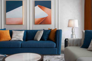 A modern living room with a blue sofa, white coffee table, and abstract art on the wall.