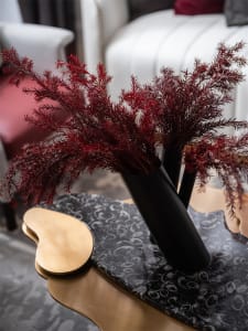 A modern decorative arrangement featuring red leaves in black metal cylinders placed on a black marble surface.