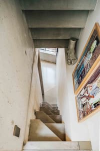 Concrete stairs leading up to a modern interior space with a concrete wall and a framed picture on the wall.