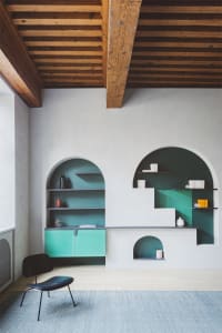 A minimalist living room with white walls, green shelves, and concrete and wooden furniture.