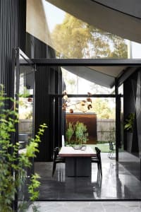 A modern dining room featuring concrete folding doors, a wooden dining table, and a unique pendant light hanging from the cei