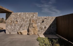 A modern outdoor space featuring a stone wall with large boulders integrated into the design, set against a clear blue sky.