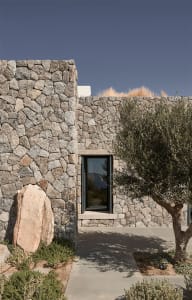 A residential house with walls constructed of irregularly shaped stone blocks, featuring a single glass door and a pathway le