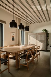 A modern minimalist dining room featuring a wooden table and chairs, with a wooden ceiling and pendant lights