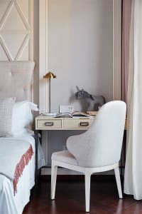 A minimalist office desk space featuring a wooden desk with a brass lamp, a unicorn plush toy, and an open book, alongside a 