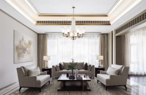 A modern living room with neutral-toned fabric furniture, light wood accents, and large windows with white curtains.