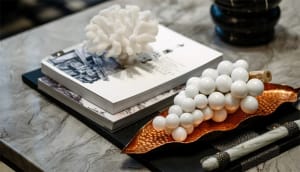 Decorative white spheres arranged on a metal plate, placed on a marble table with books and coral decor.