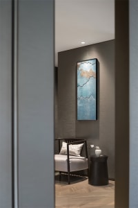 Modern minimalist lounge area with glass accent wall, comfortable seating, and elegant artistic piece